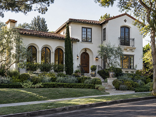 Mediterranean Revival house in white stucco with a red tile roof, arched openings and arched wood casement windows