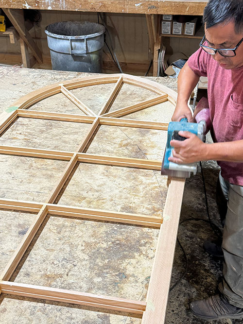 Sanding a new arched divided-light sash in the shop